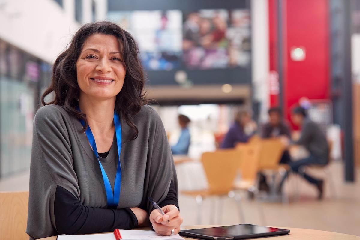 Portrait Of Mature Female Teacher Or Student With Digital Tablet Working At Table In College Hall